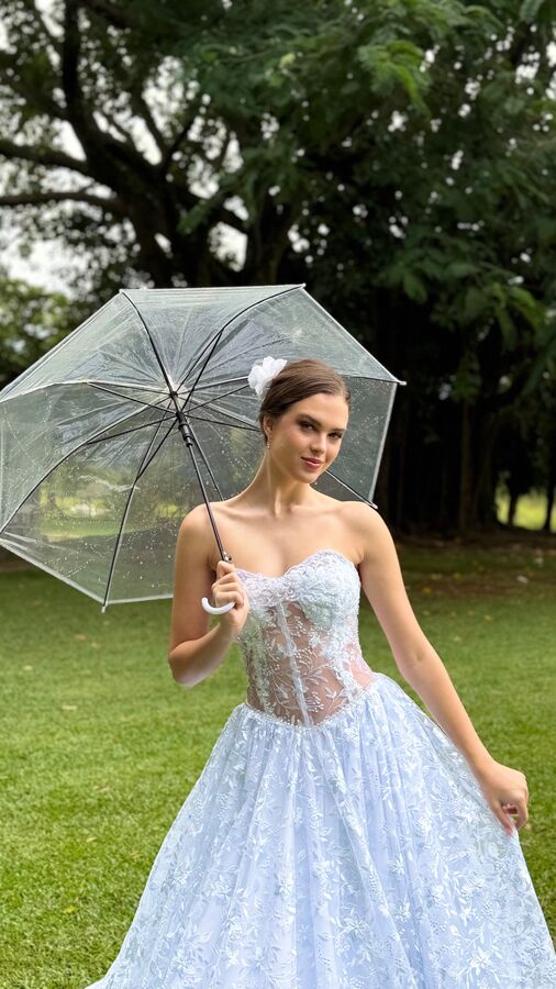 Mulher com guarda-chuva transparente e vestido azul rendado em um jardim