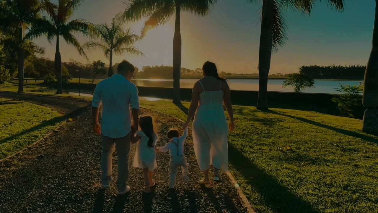 Família caminhando entre palmeiras ao pôr do sol, à beira de um lago