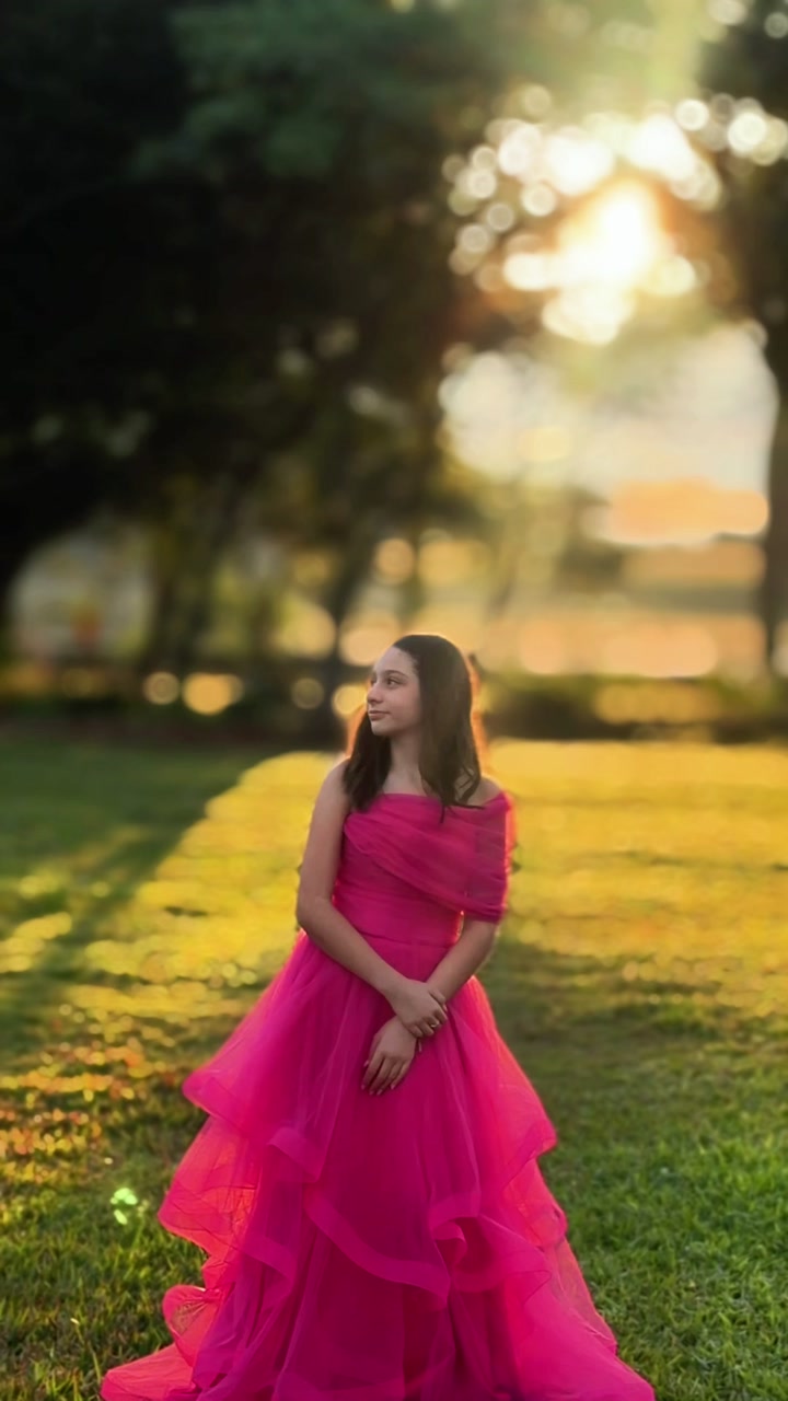 Mulher com vestido pink volumoso em um gramado, com o sol entre as árvores