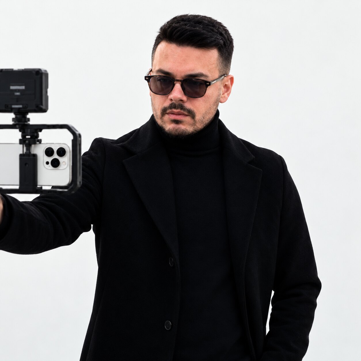 Rayllan de casaco preto e óculos escuros, segurando um rig de celular com monitor
